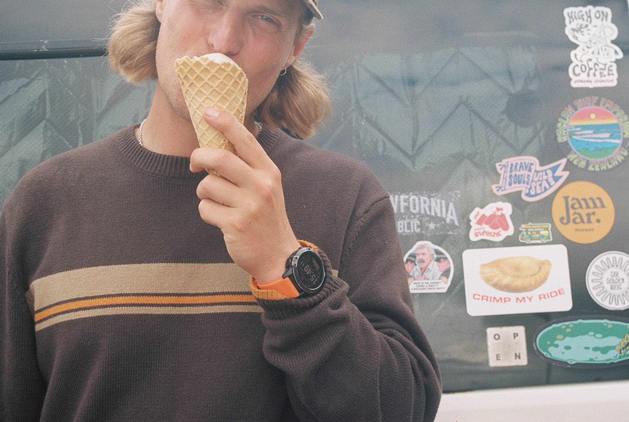 Person eating an ice cream cone in front of a car with various stickers.