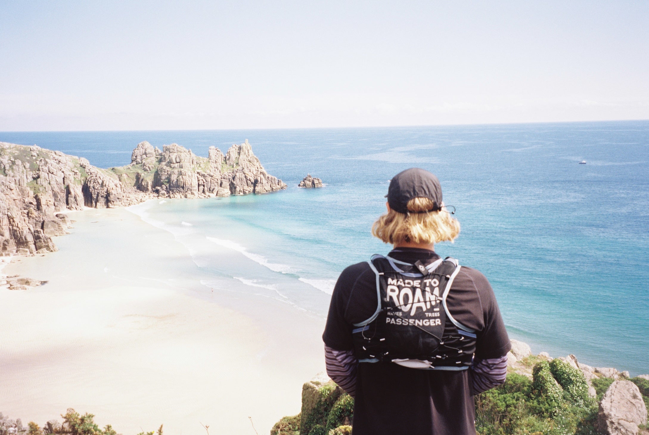 Person wearing a black jacket with 'Made to Roam' branding overlooking a scenic coastal view.