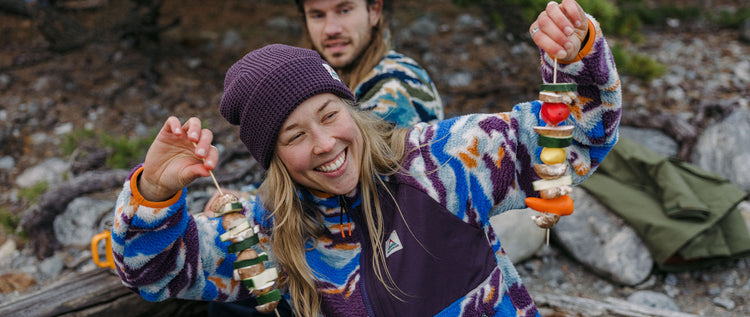 A woman in fleece and beanie, holding veggie skewers