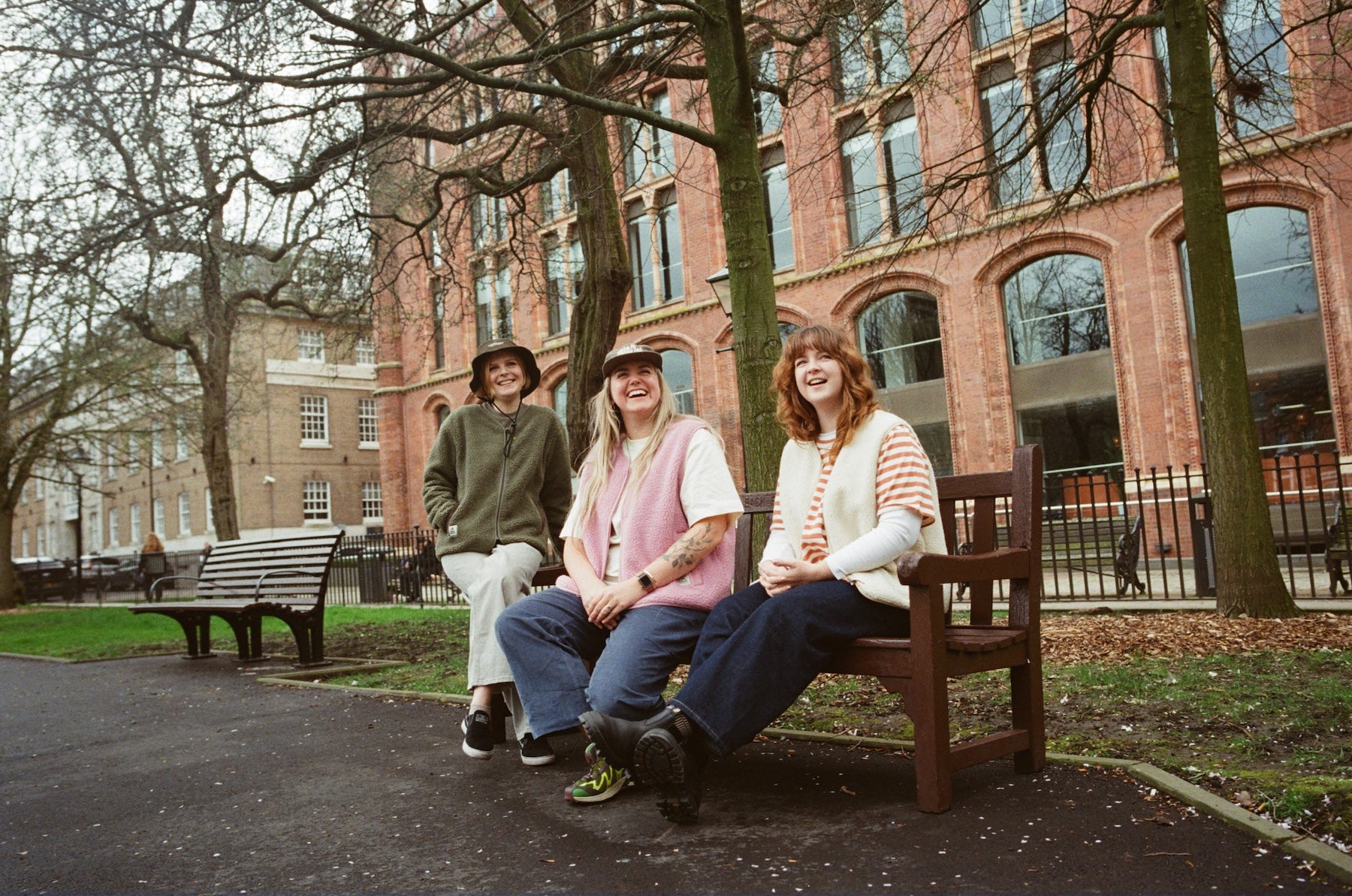 Three women sitting on a bench in front of a brick building